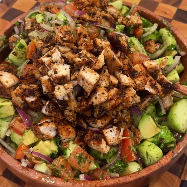 Grilled chicken salad with fresh vegetables and herbs in a wooden bowl.