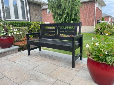 Black wooden bench on a stone patio surrounded by plants.