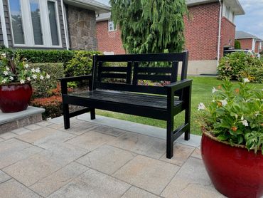 Black wooden bench on a patio surrounded by greenery and red flower pots.