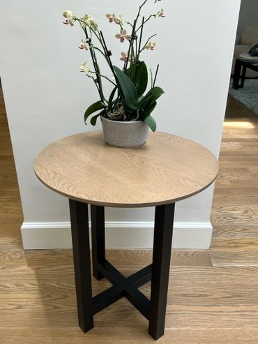 Round wooden table with black legs holding a potted orchid.