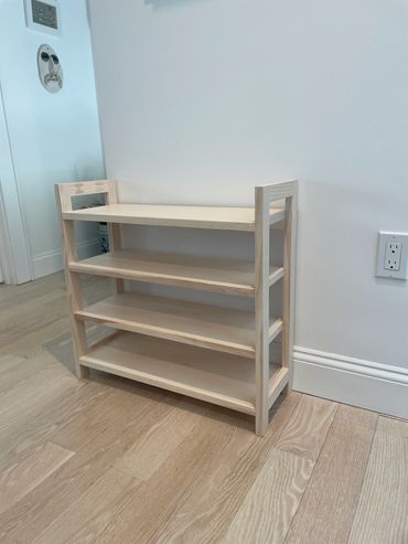 A simple, light wooden shelf with three tiers against a white wall.