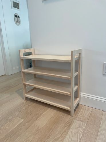 Minimalist light wood shelf unit with four tiers in a room corner.