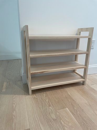 A simple wooden four-tier shelf standing on a wooden floor.