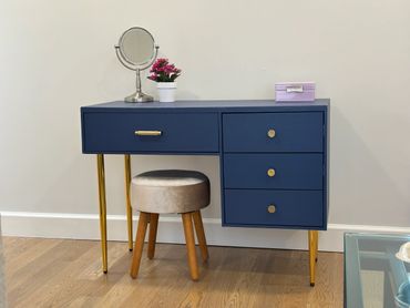 Modern blue vanity table with gold legs and a small round stool.
