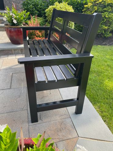 Black wooden bench on a patio next to green lawn and plants.