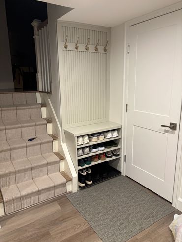 Organized shoe rack and coat hooks by carpeted stairs and white door.