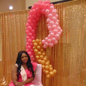 Lady in pink dress sitting in front of a balloon backdrop.