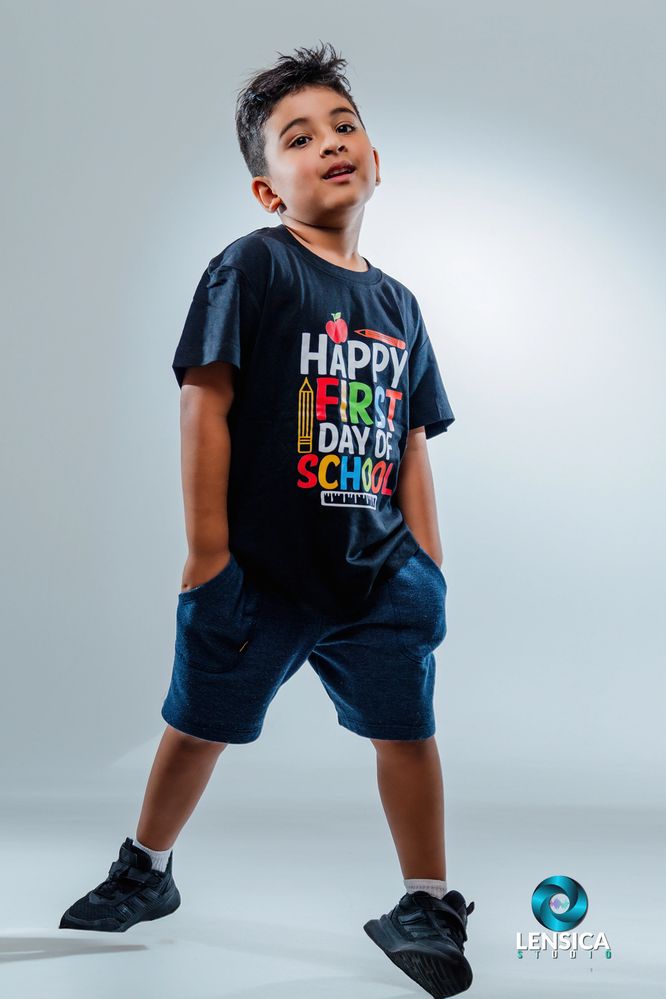 Young boy posing confidently in a colorful first day of school t-shirt and shorts.
