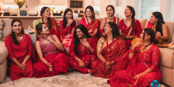 A joyful group of women dressed in red traditional attire, sharing laughter indoors.