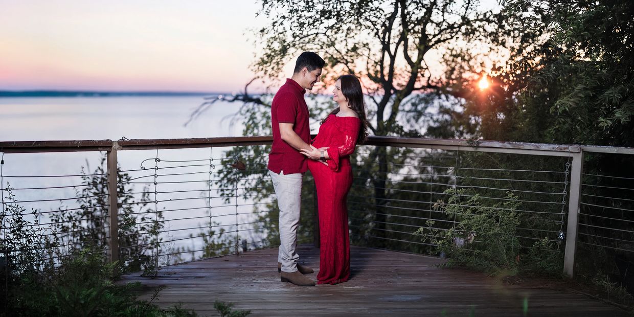 A couple in red outfits sharing a moment at sunset on a wooden deck near water.