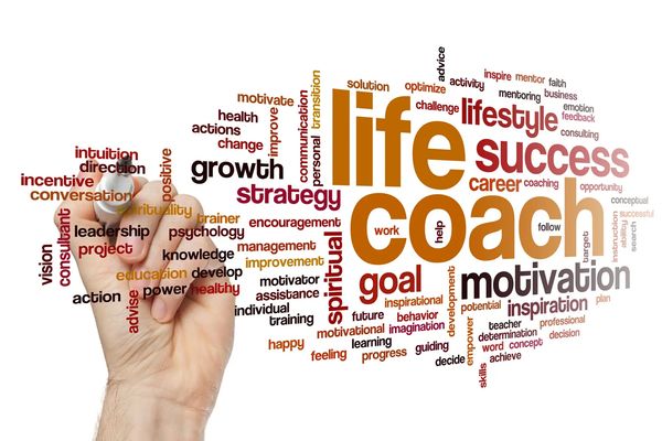 A hand holding a marker creates a word cloud featuring "life coach", "success", "motivation"
