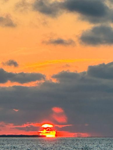 Sun setting below a cloudy sky over the ocean.