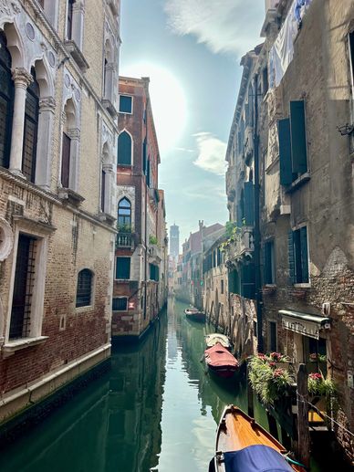 Sunlit canal with boats between old Venetian buildings.