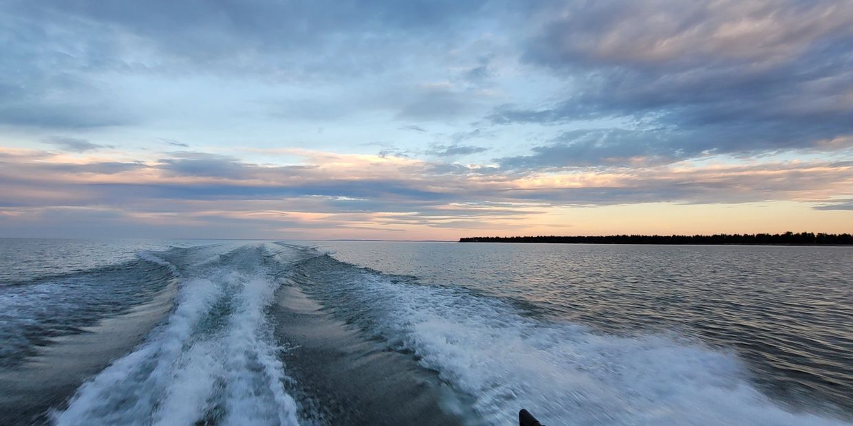Boat wake trailing on calm water under a colorful sunset sky.
