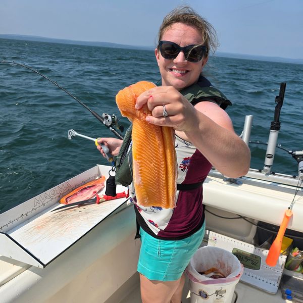 Woman on boat proudly holding a large salmon fillet while fishing.