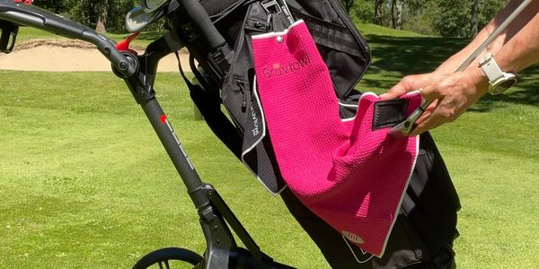 Pink Gruvtowl trifold/cart towel on a golf cart being used to clean a golf club