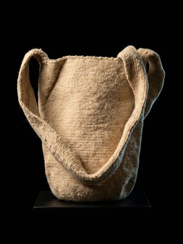 Handwoven natural fiber bag with a wide strap on black background.