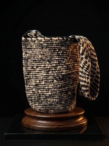 Woven basket with a handle displayed on a wooden pedestal against a black background.