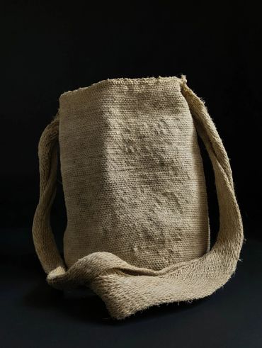 Handwoven beige shoulder bag with textured fabric against a dark background.