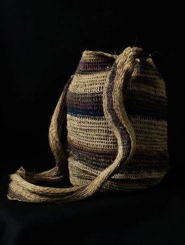 Handwoven bag with earthy tones and a long strap on a black background.