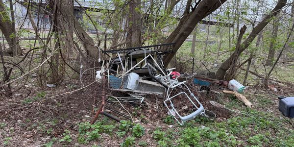 Pile of discarded metal and plastic items in a wooded area.