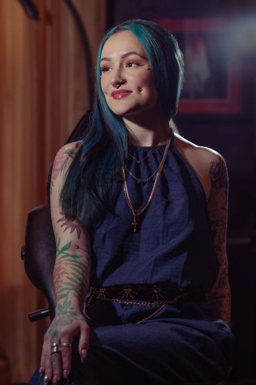 Woman with tattoos and blue hair sitting and smiling.