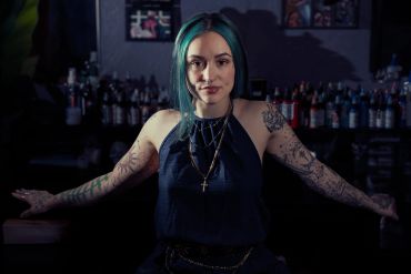 Young woman with tattoos posing confidently in a dimly lit bar.