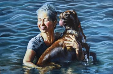 A woman joyfully hugging her dog in water with gentle waves around.