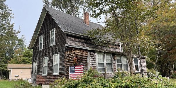 Rustic wooden house with American flag and surrounding greenery.