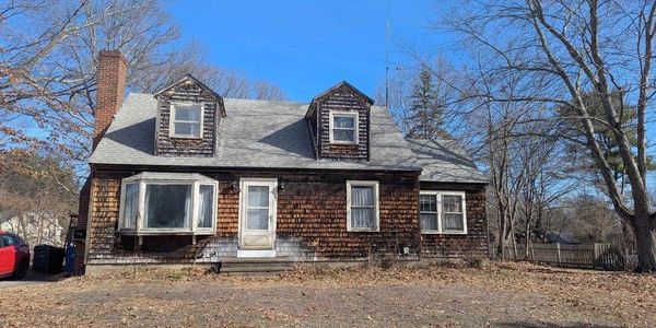 Old wooden house with a gray roof and leafless trees around it.