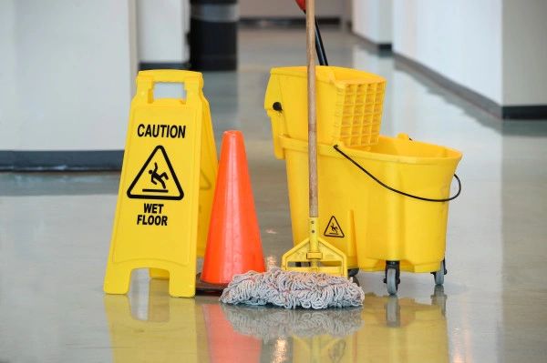 Cleaning equipment with a caution wet floor sign and mop on a shiny floor.