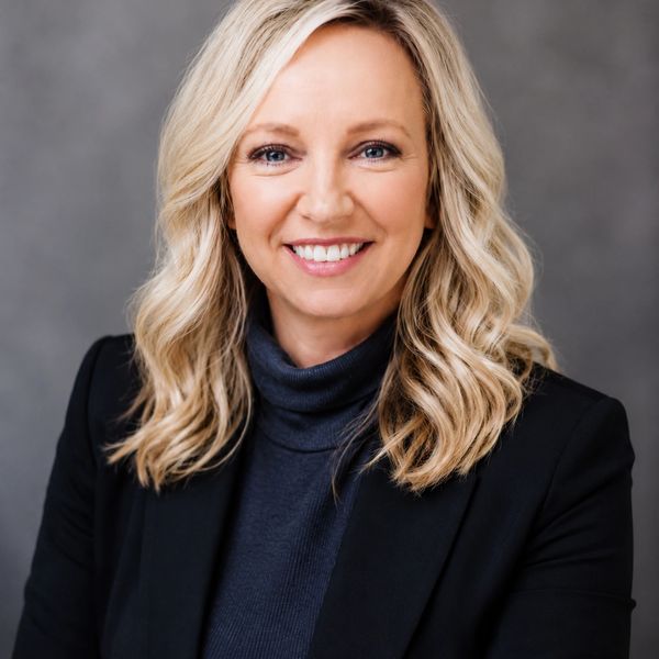 Smiling woman with blonde hair in black blazer and turtleneck.