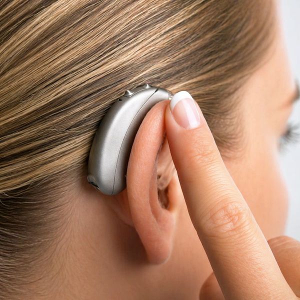 Close-up of a person adjusting a hearing aid behind their ear.