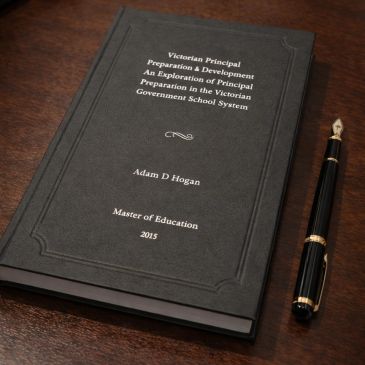 A black hardcover thesis titled 'Victorian Principal Preparation &amp; Development' with a fountain pen beside it.
