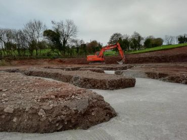 Excavator working on a construction site with dug earth and concrete base.