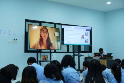 Students attending a virtual lecture displayed on large screens in a classroom.
