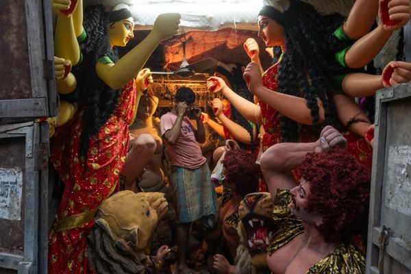 Artisans sculpting large, colorful statues of Hindu deities in a narrow workshop.