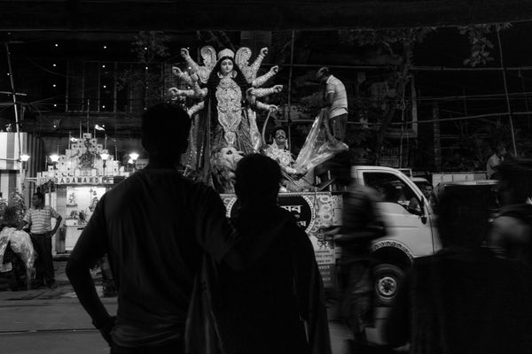 People silhouetted against a large statue of a multi-armed goddess at night.