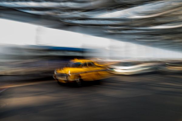 Blurred image of a yellow taxi moving fast under a roof.