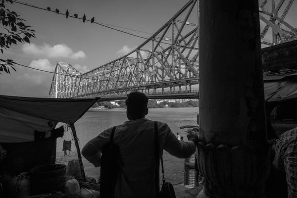 A person looks out at a large bridge over a river in black and white.