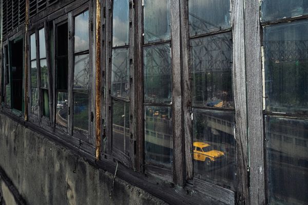 Reflection of a yellow car in old, weathered windows.