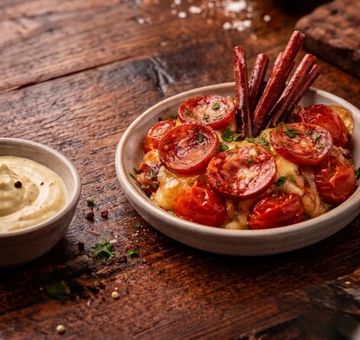 Baked tomatoes with melted cheese and sausage sticks served with a creamy dip.