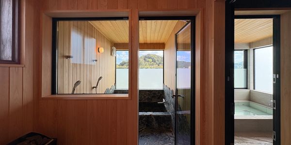 Wood-paneled sauna and adjacent bathing area with views of nature.
