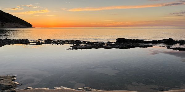 Sunset over a calm rocky beach with gentle waves.
