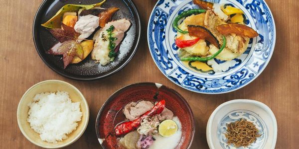 A traditional Japanese meal with rice, fish, vegetables, and pickled items on elegant plates.