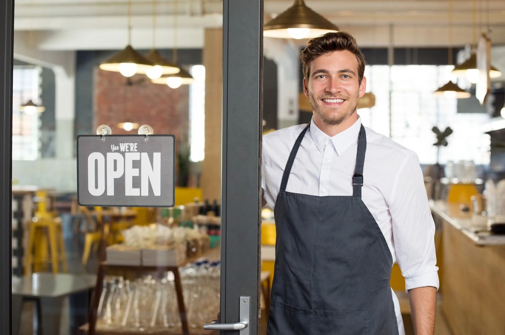 Smiling barista stands by an open cafe door.