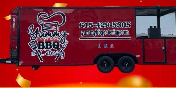 Mobile BBQ catering trailer with branding and contact info.