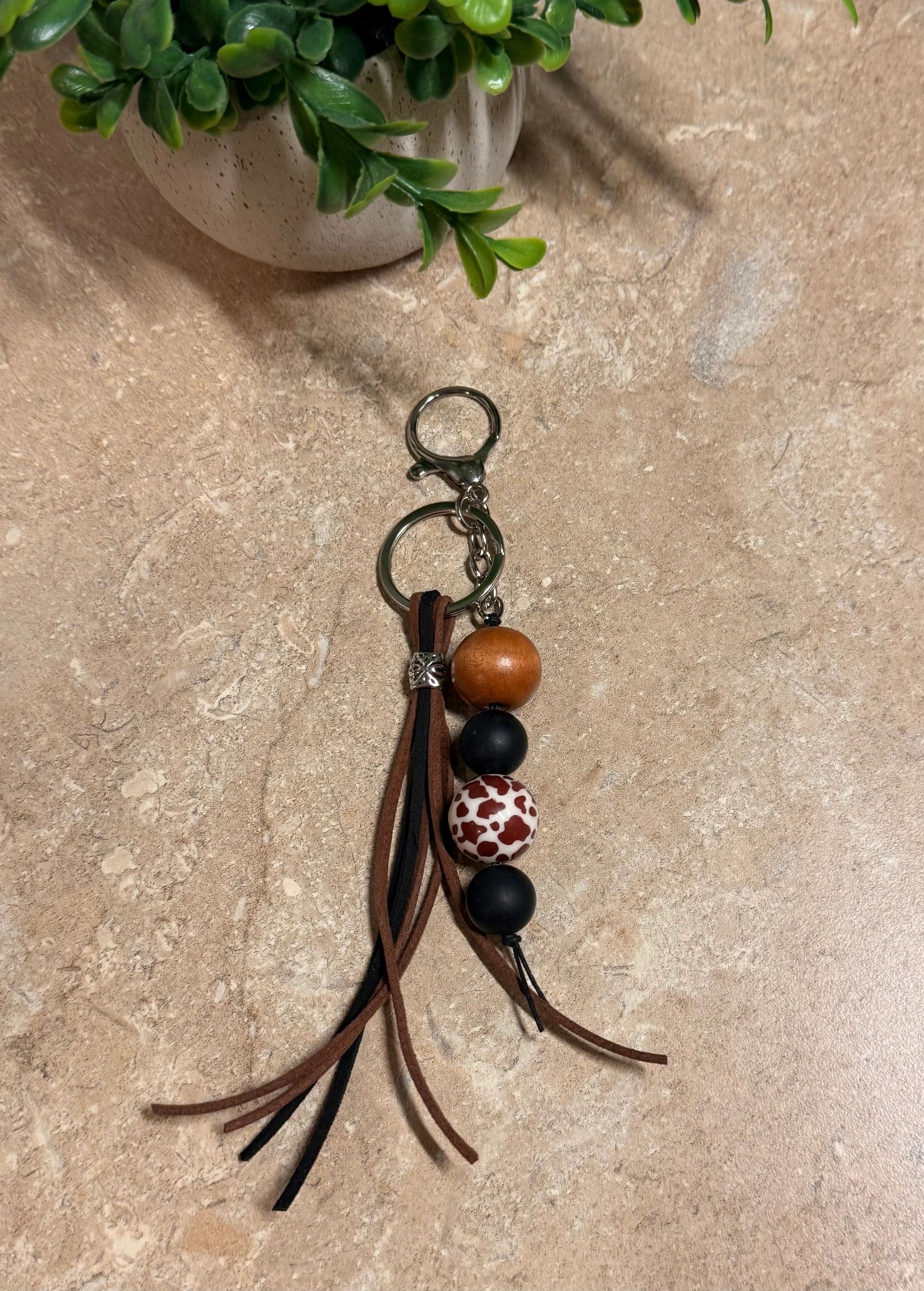 Purse charm with wooden, black and cow print beads with leather tassel on silver keyring.
