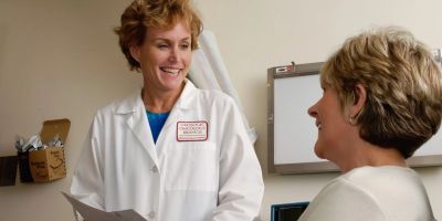 A doctor in a white coat discusses medical paperwork with a patient during an appointment.