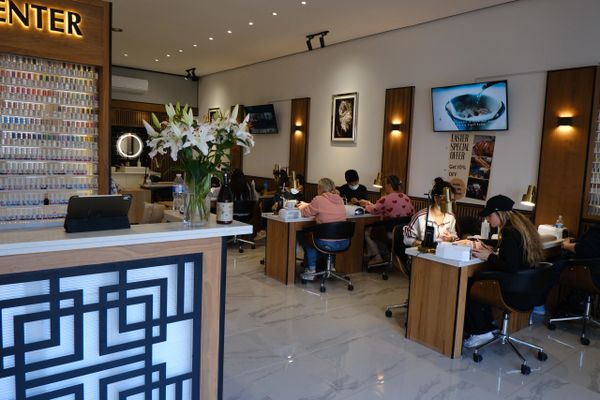 Modern nail salon with clients getting manicures at wooden tables.